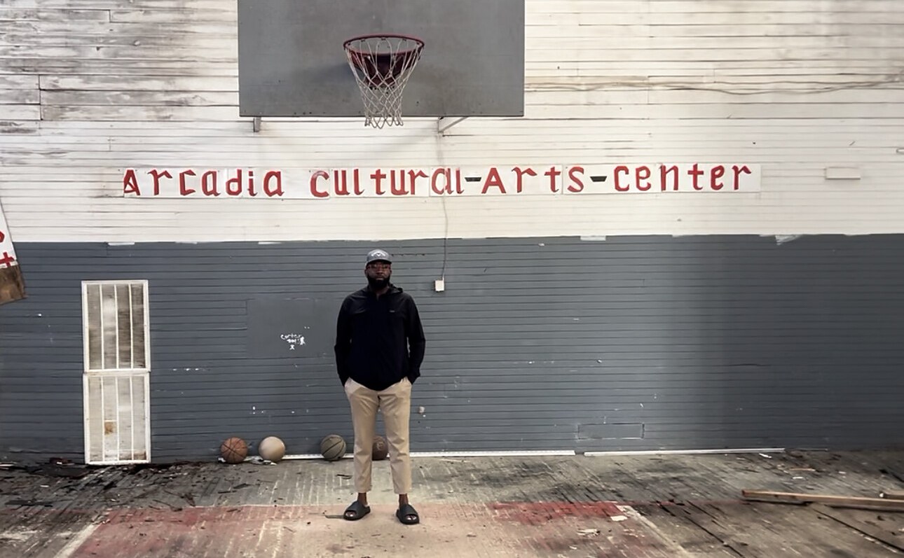 Dr. Andrews standing beneath the basketball hoop of the Arcadia Cultural Arts Center, East Arcadia, NC